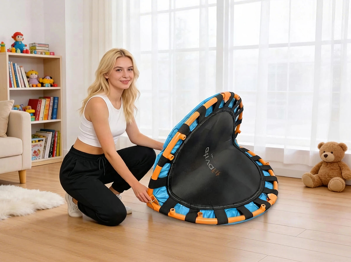 Woman holding a black and orange exercise trampoline in a room with a bookshelf and teddy bear.