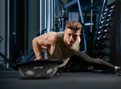 Man performing push-ups on a black massage half balance ball in a gym setting